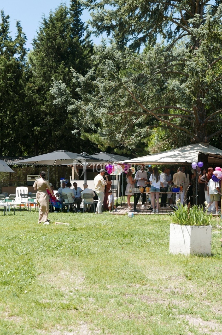 Groupe de personnes réunies dans un jardin, près de tables et d'un chapiteau, entouré d'arbres et de verdure.