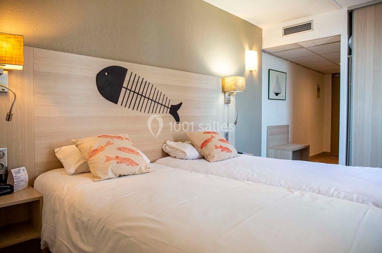 Deux lits simples avec tête de lit en bois décorée d'un motif de poisson, dans une chambre lumineuse et moderne.