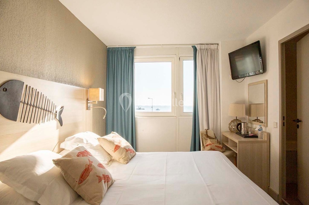 Chambre lumineuse avec lit double, décoration marine, fenêtre donnant sur une vue extérieure et télévision murale.