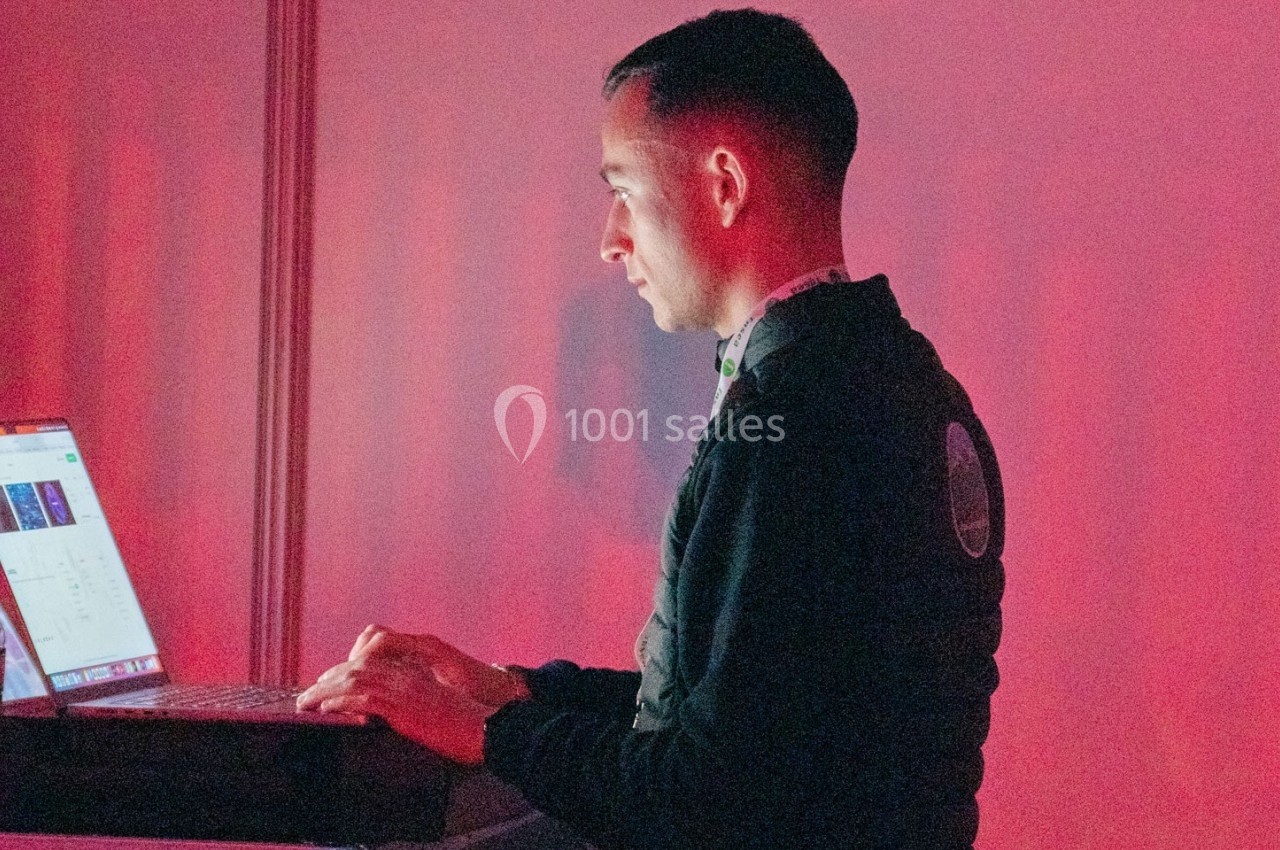 Un homme utilise un ordinateur portable dans un environnement éclairé par une lumière rouge.