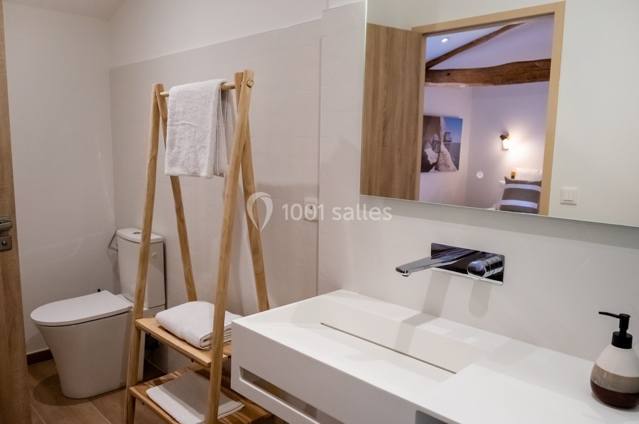 Salle de bain moderne avec lavabo blanc, miroir, étagère en bois, toilettes et serviettes pliées.