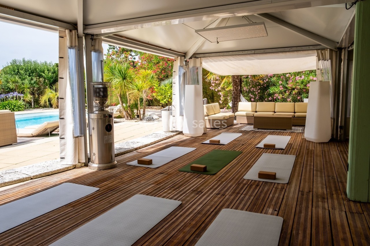 Salle ouverte avec tapis de yoga, briques en bois et vue sur un jardin avec piscine.