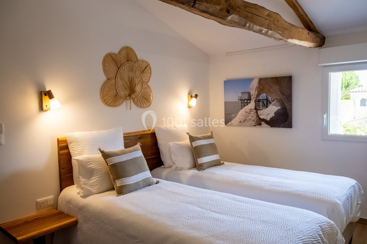 Deux lits simples avec linge blanc dans une chambre lumineuse, décorée de poutres apparentes et d'éléments naturels.