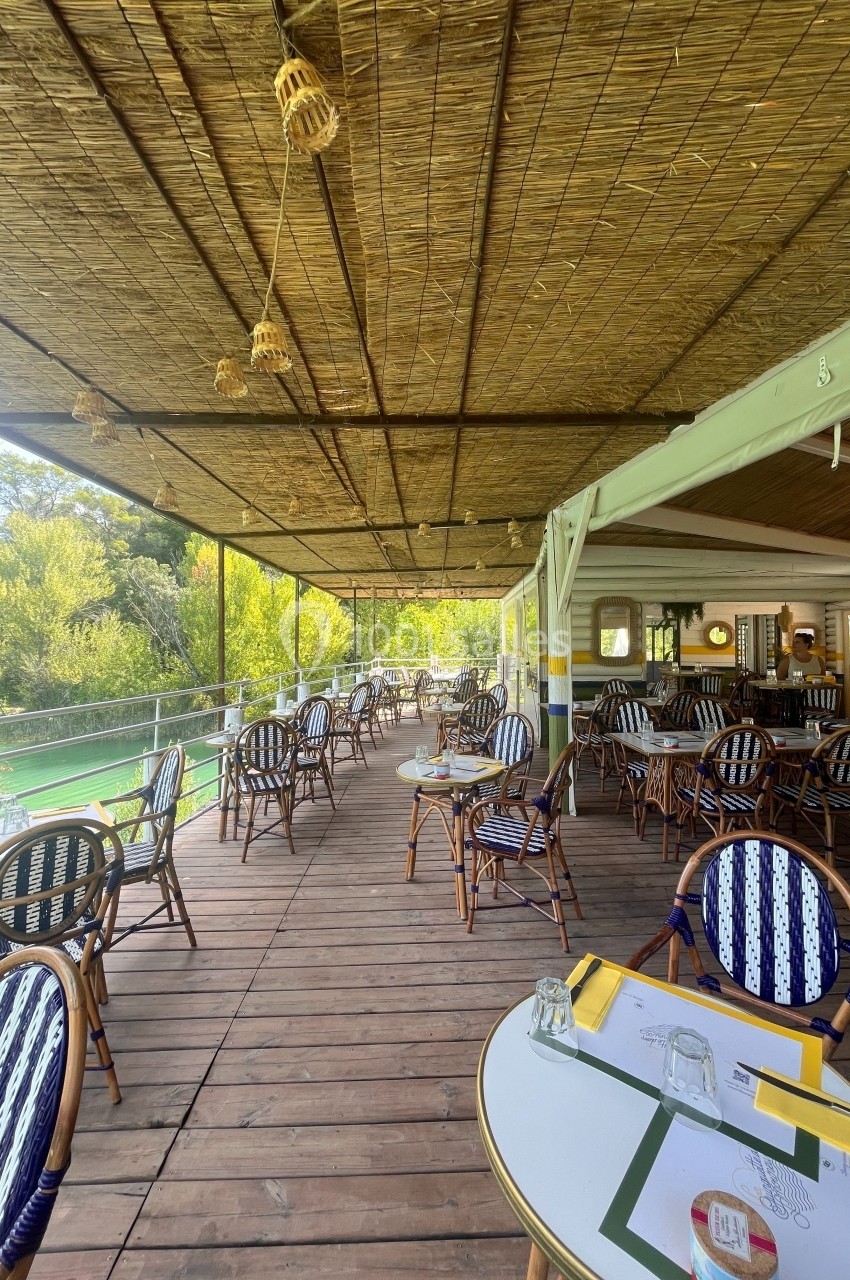 Terrasse en bois d'un restaurant avec des tables et chaises en osier, vue sur un environnement verdoyant.