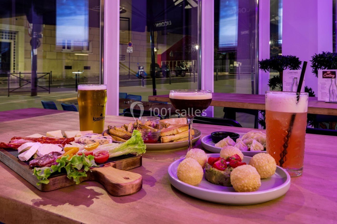 Assortiment de plats et boissons sur une table en bois dans un restaurant avec vue sur des fenêtres donnant sur la rue.