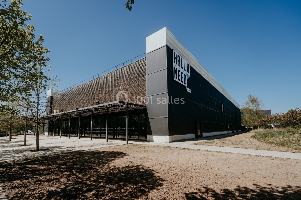 Bâtiment moderne avec façade en bois et métal, entouré d'arbres et d'une allée pavée sous un ciel dégagé.