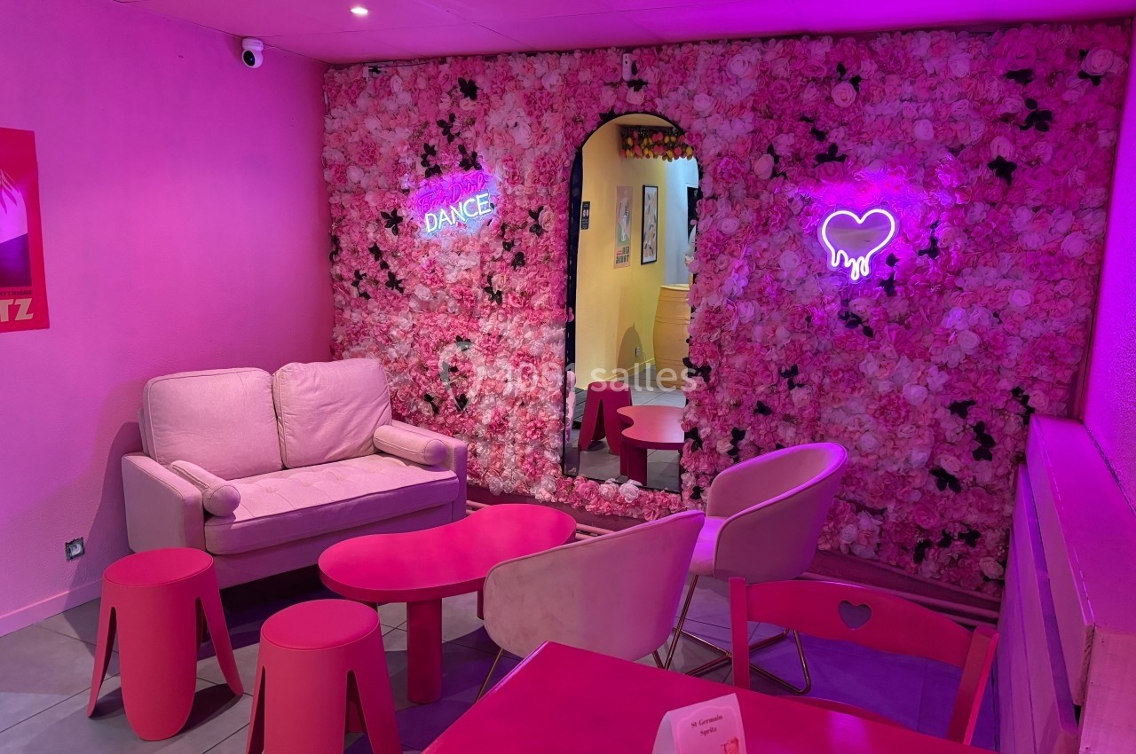 Salon décoré de tons roses avec un mur floral, néons lumineux et mobilier assorti, créant une ambiance chaleureuse.