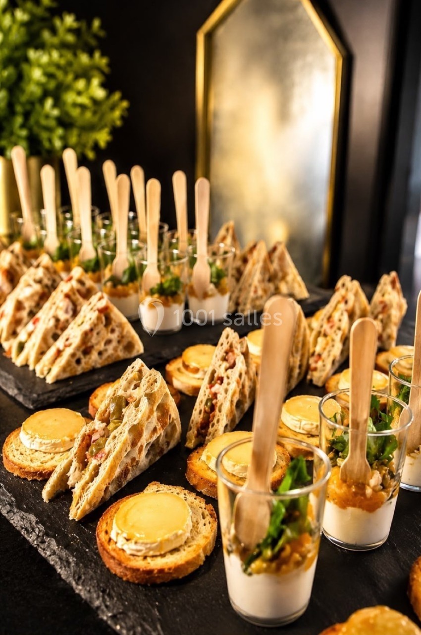 Plateau de bouchées apéritives variées comprenant toasts, verrines et mini-sandwichs, présenté sur ardoises noires.