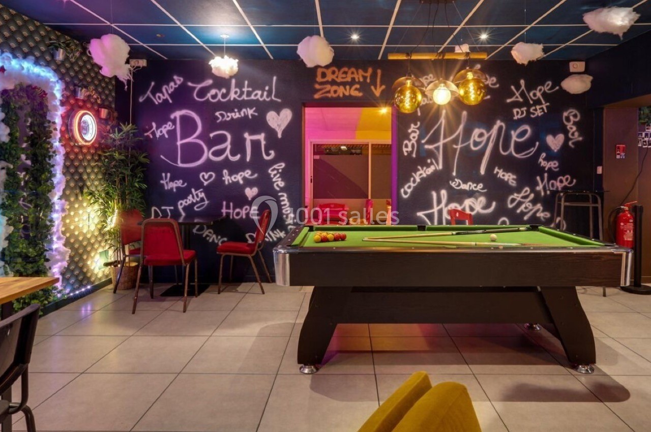 Salle de loisirs avec table de billard, murs décorés de graffitis lumineux et ambiance colorée.