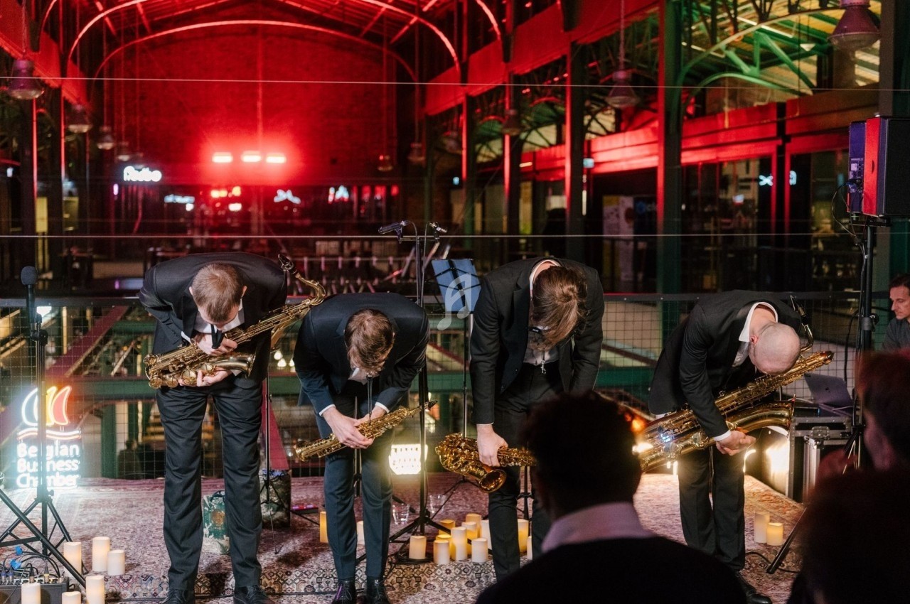 Quatre musiciens en costume saluent sur une scène éclairée, entourés de bougies, dans un espace intérieur industriel.