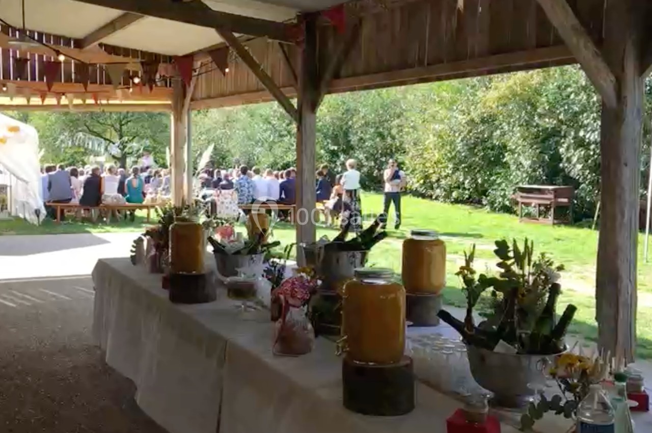 Buffet en extérieur sous un abri en bois, avec des invités assis au loin dans un jardin verdoyant.