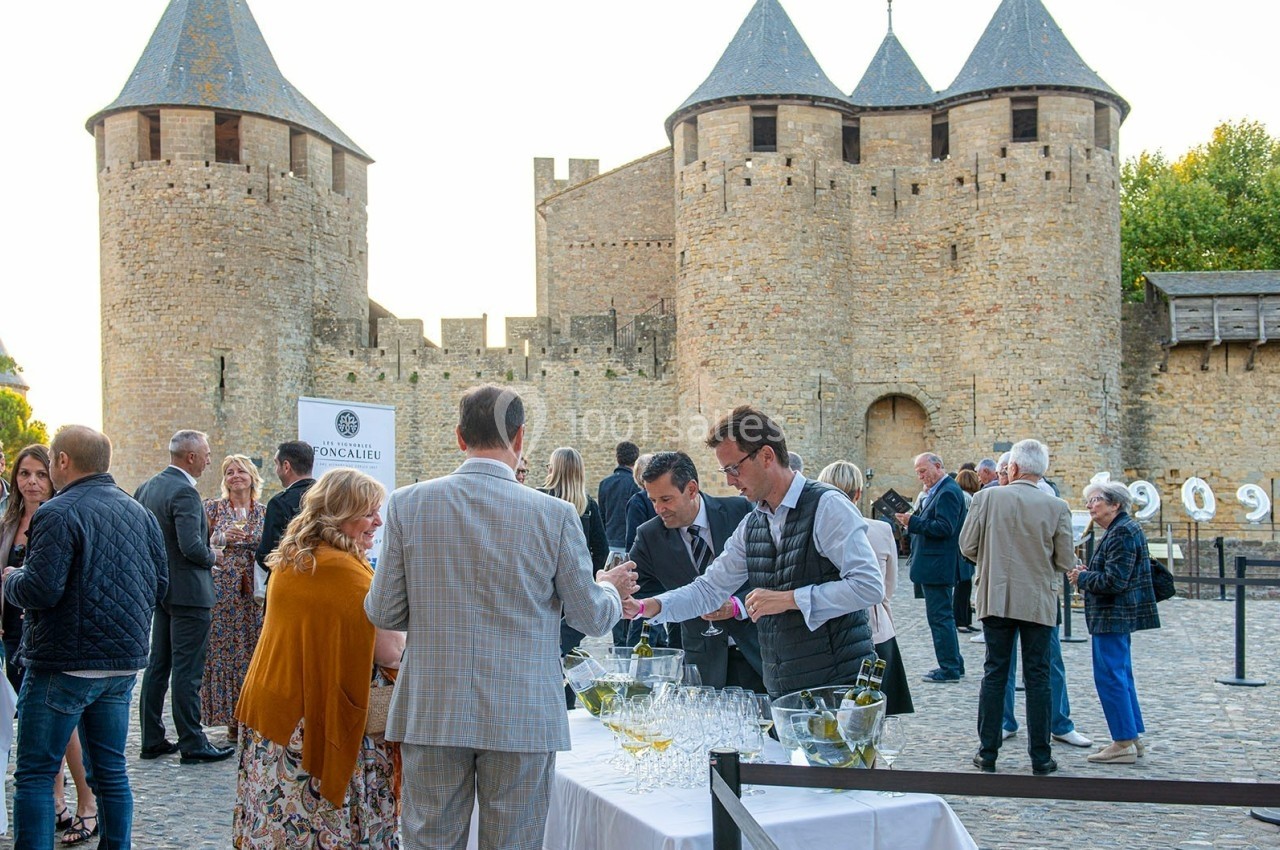 Des personnes rassemblées devant les remparts d'un château médiéval, lors d'un événement en plein air avec service de…