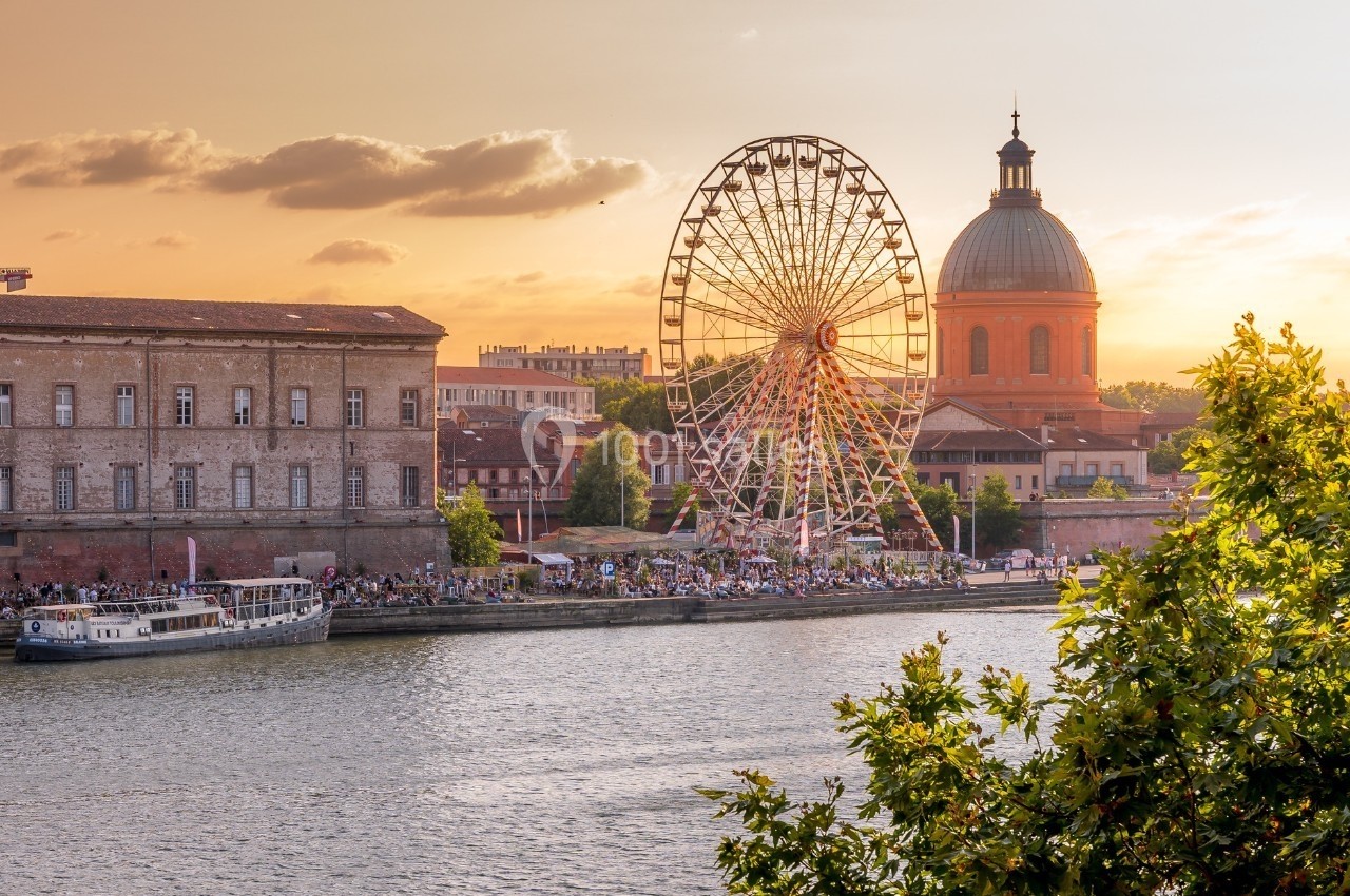 Vue sur une grande roue, un dôme et des bâtiments historiques au bord d'une rivière au coucher du soleil.