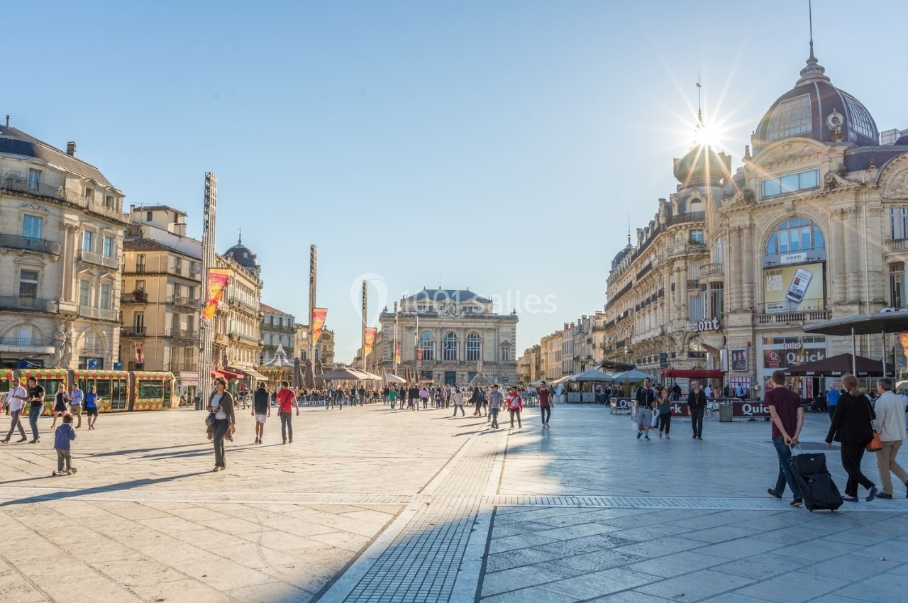 Place animée avec passants, bâtiments historiques et soleil éclatant au-dessus d'une architecture classique.