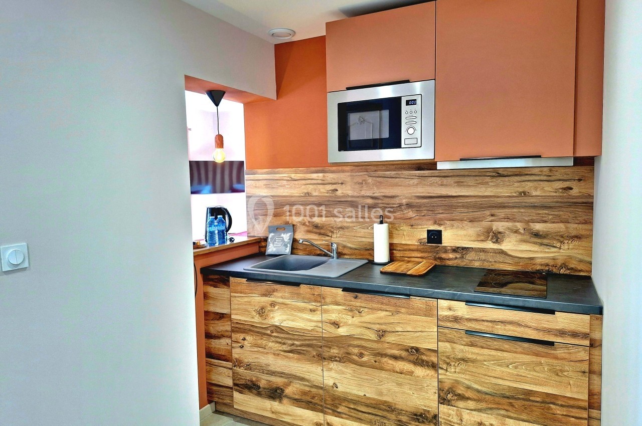 Cuisine moderne avec placards en bois, plan de travail sombre, évier, micro-ondes intégré et éclairage suspendu.