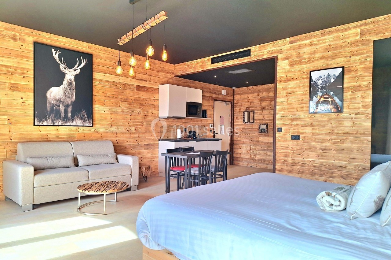 Chambre moderne en bois avec lit, canapé, coin cuisine, table à manger et décorations murales.