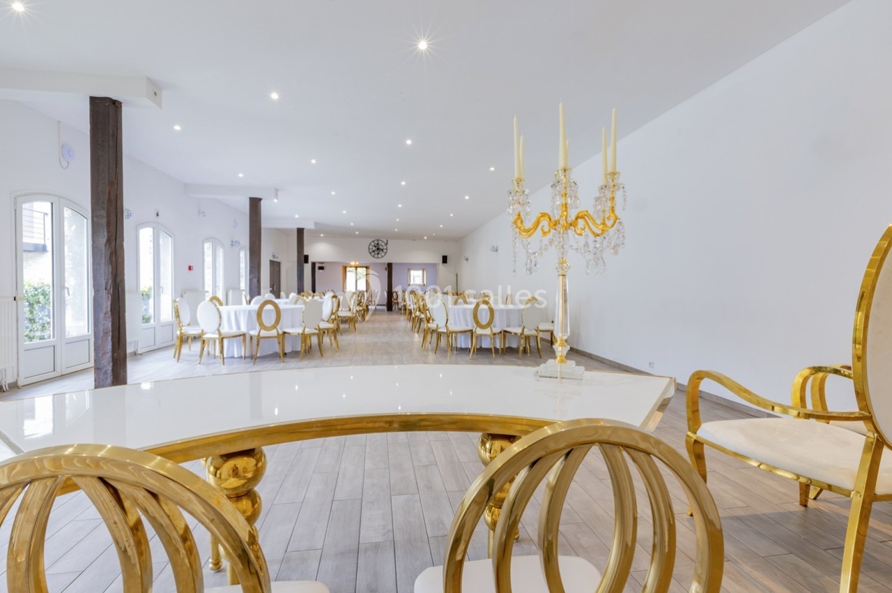 Salle de réception lumineuse avec tables et chaises dorées, décorée d'un chandelier élégant sur une table blanche.