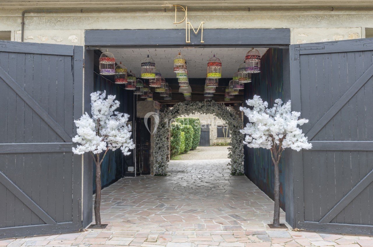 Entrée décorée avec des portes ouvertes, des arbres artificiels blancs et des cages suspendues colorées.