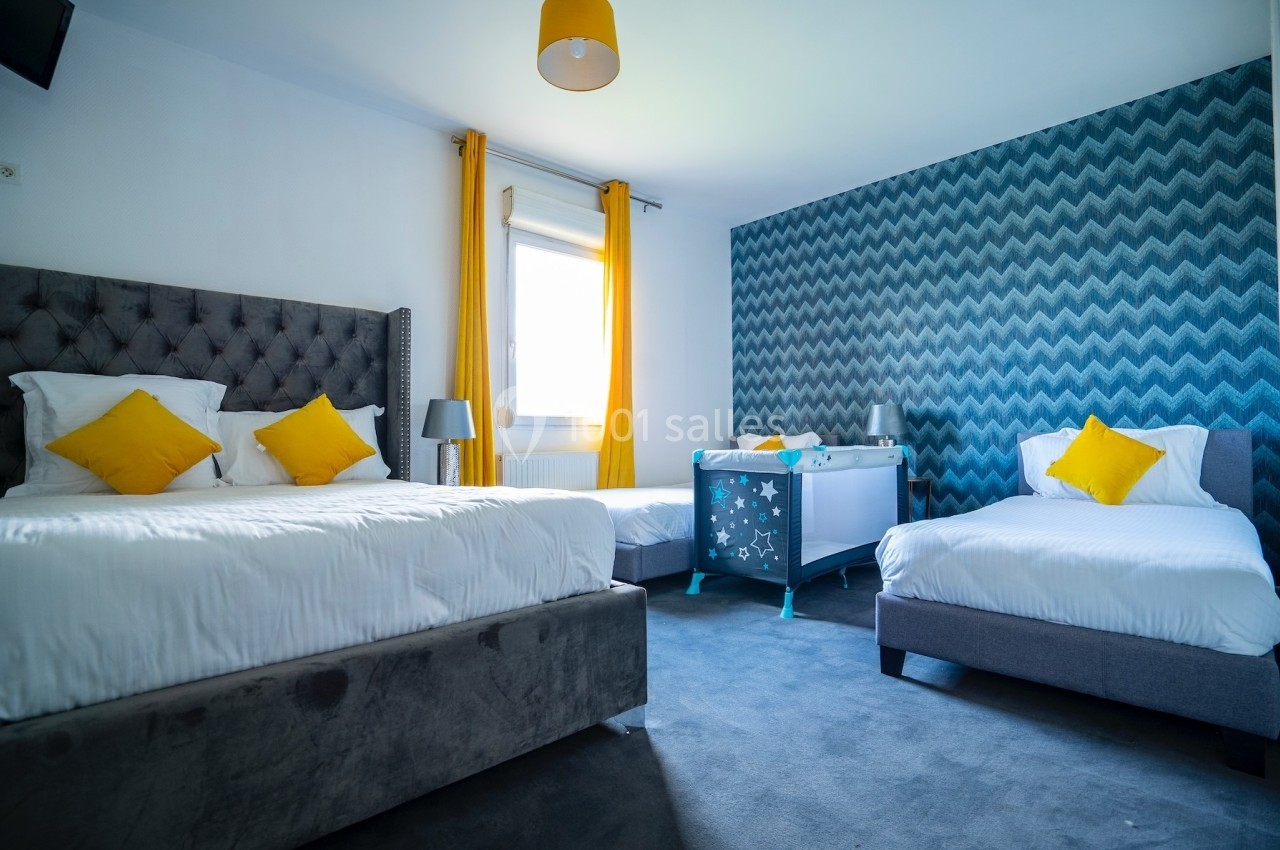 Chambre lumineuse avec deux lits simples, un lit double, un berceau et une décoration murale à motifs géométriques.