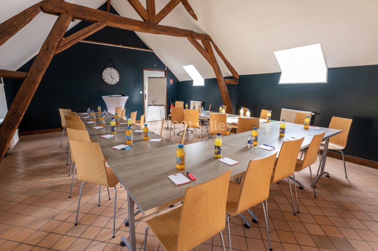 Salle de réunion lumineuse avec tables en U, chaises en bois, bouteilles d'eau et blocs-notes disposés pour les participants.