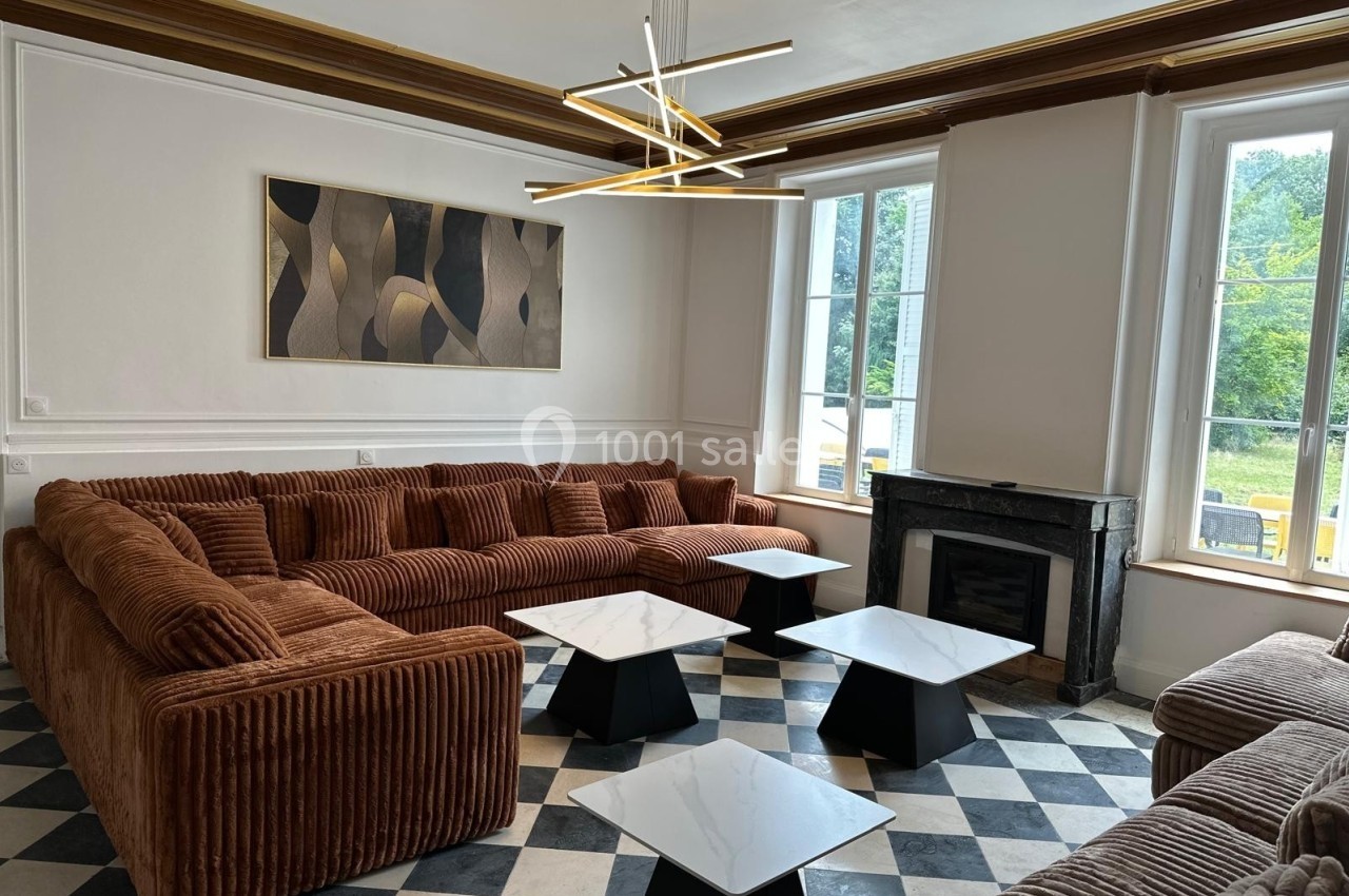Salon lumineux avec canapé en velours marron, tables basses en marbre, cheminée noire et grandes fenêtres donnant sur un…