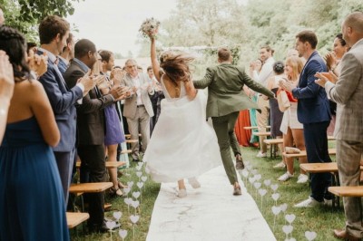 Un couple de mariés joyeux quitte une cérémonie en plein air sous les applaudissements des invités.