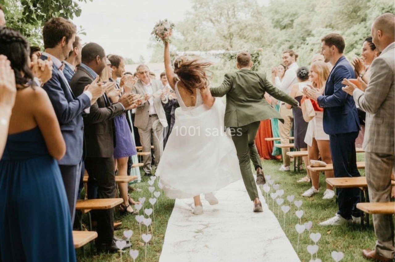 Un couple de mariés joyeux quitte une cérémonie en plein air sous les applaudissements des invités.