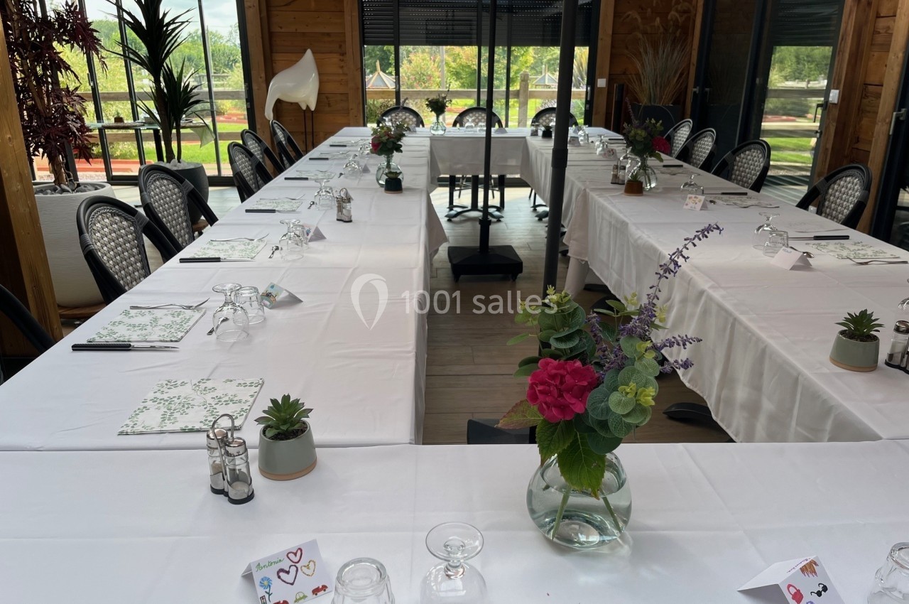 Salle de réunion lumineuse avec tables disposées en U, nappes blanches, décorations florales et vue sur l'extérieur…
