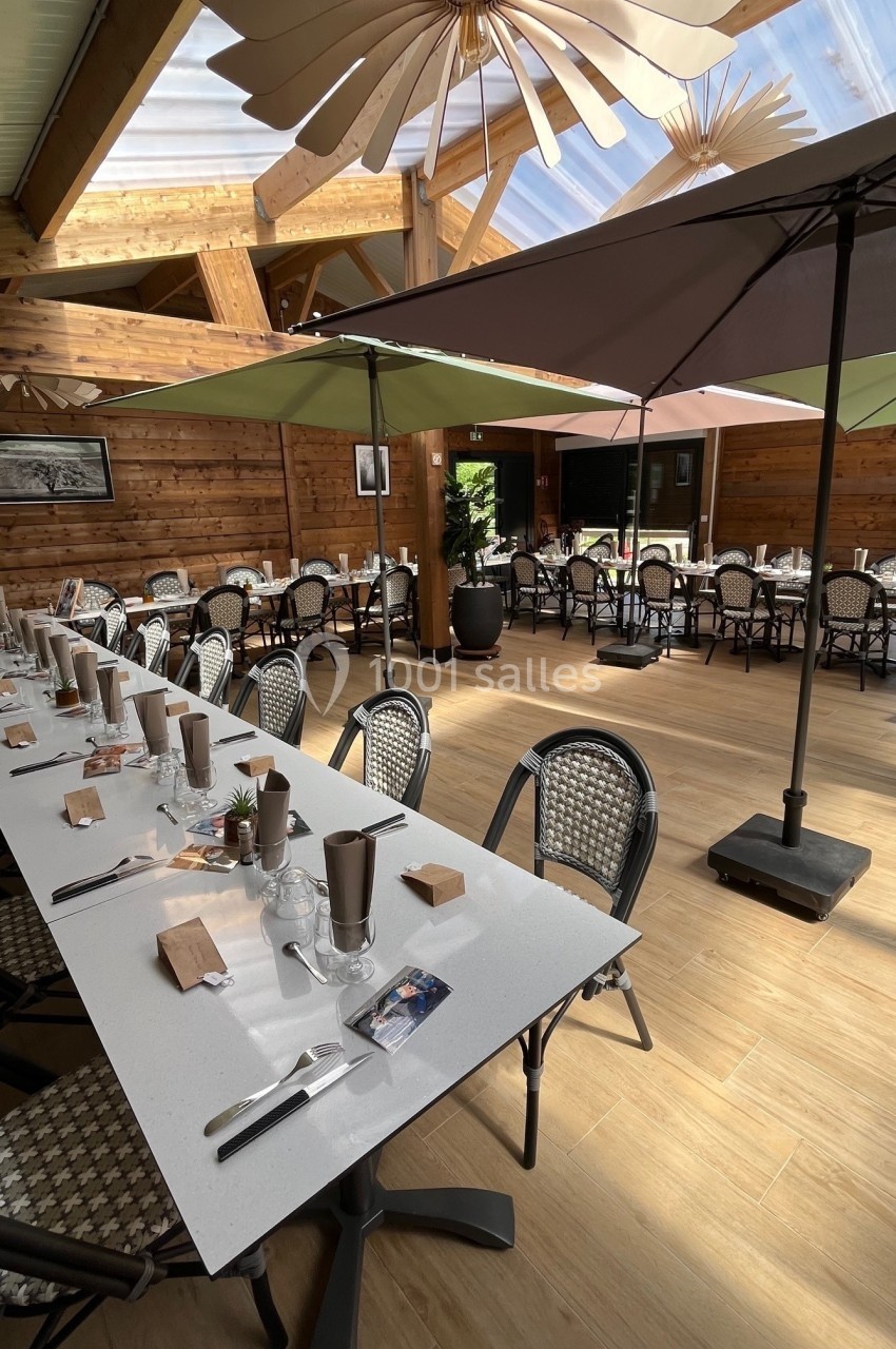 Salle de restaurant lumineuse avec tables dressées, chaises en osier, parasols et décoration en bois.