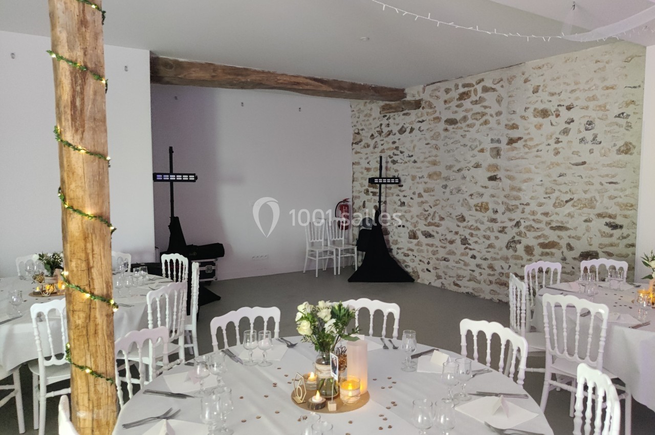 Salle de réception décorée avec des tables rondes, des chaises blanches, des fleurs et un éclairage tamisé.