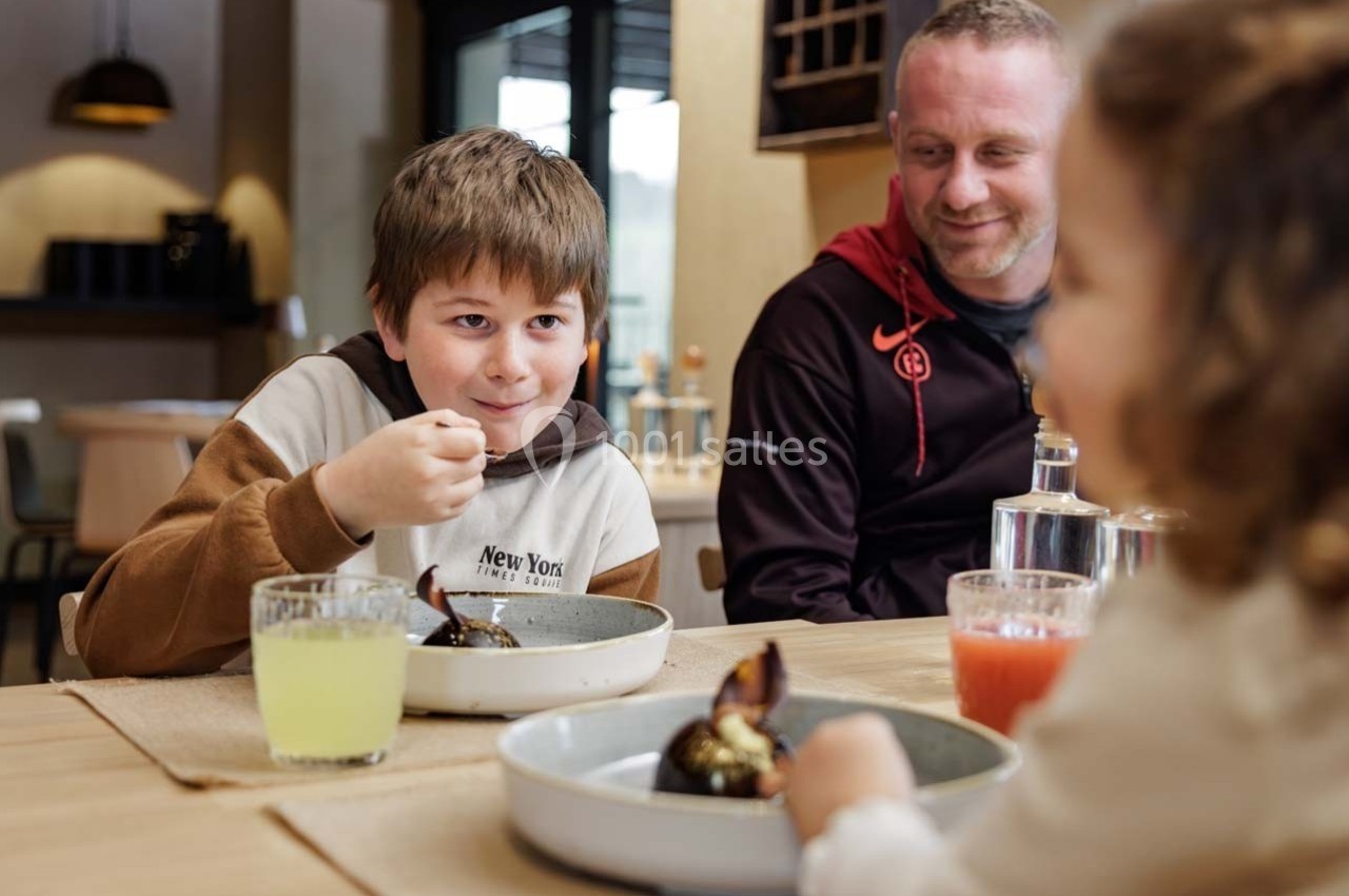 Un garçon mange un dessert à table avec un homme et une fille dans un cadre chaleureux et lumineux.