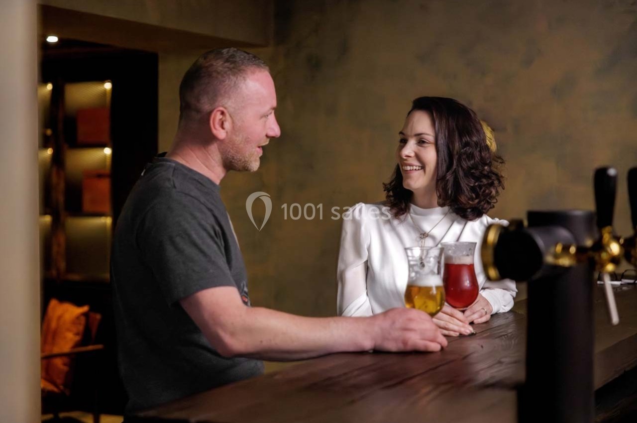 Un homme et une femme discutent en souriant autour de boissons dans un bar à l'ambiance chaleureuse.