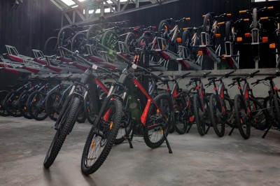 Rangée de vélos électriques noirs et rouges alignés dans un entrepôt avec des supports de rangement en arrière-plan.