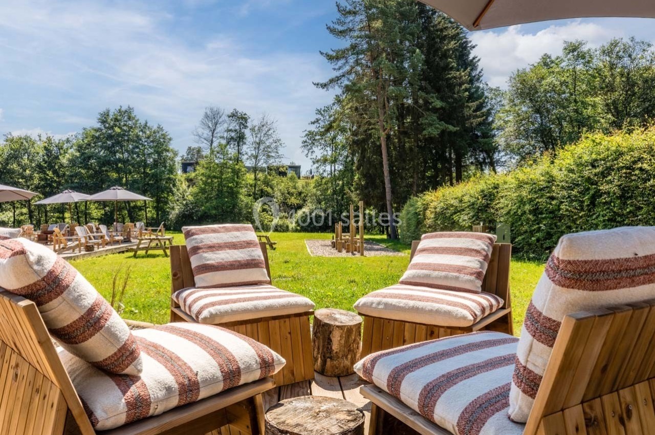 Chaises longues avec coussins rayés disposées autour d'une table en bois, dans un jardin verdoyant sous un ciel bleu.