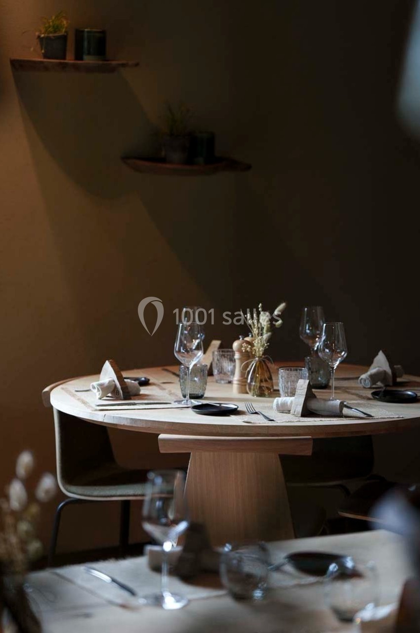 Table ronde en bois dressée avec verres, assiettes et décorations minimalistes dans une ambiance tamisée.