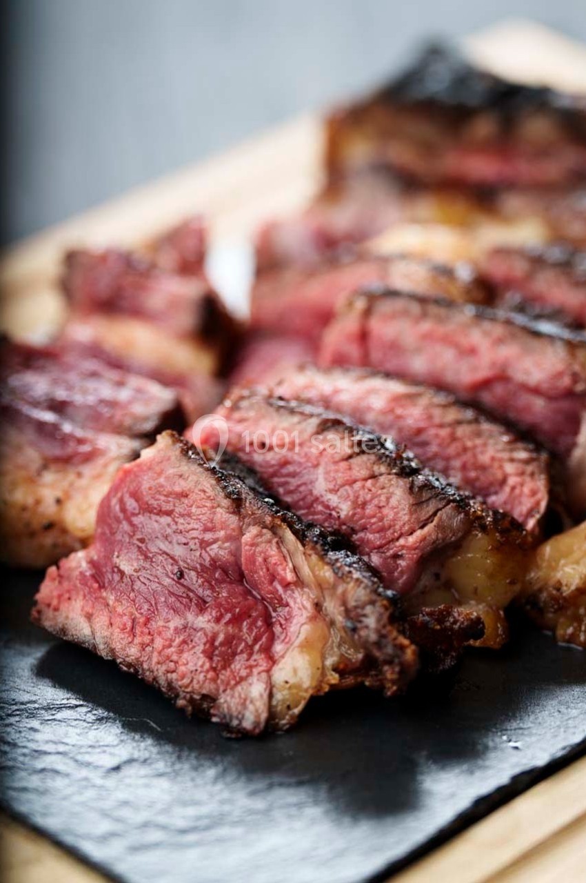 Tranches de viande grillée saignante disposées sur une planche en ardoise.