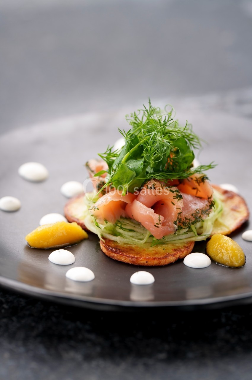Assiette garnie de saumon fumé, salade verte, herbes fraîches, tranches de pommes de terre et sauces disposées autour.