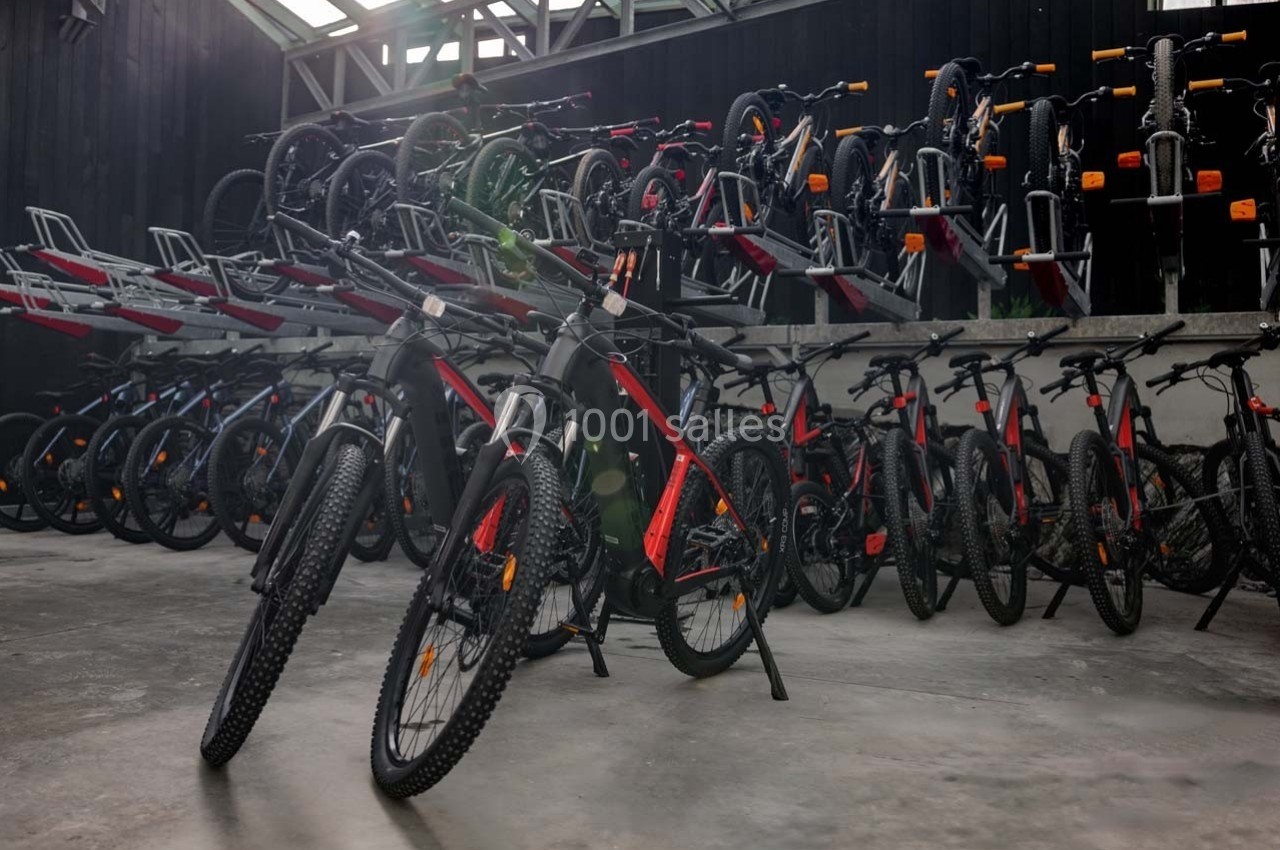 Rangée de vélos électriques noirs et rouges alignés dans un entrepôt avec des supports de rangement en arrière-plan.