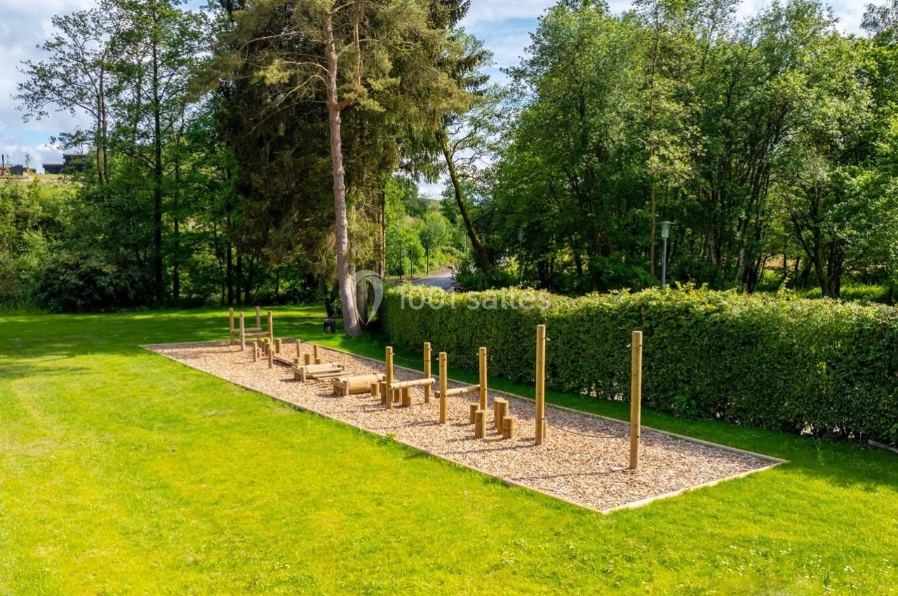 Parcours d'exercice en plein air avec équipements en bois, entouré de pelouse et d'arbres.