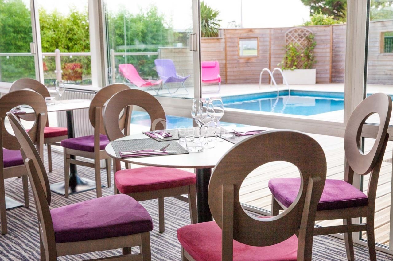 Salle à manger lumineuse avec vue sur une piscine extérieure, table dressée et chaises aux coussins roses.