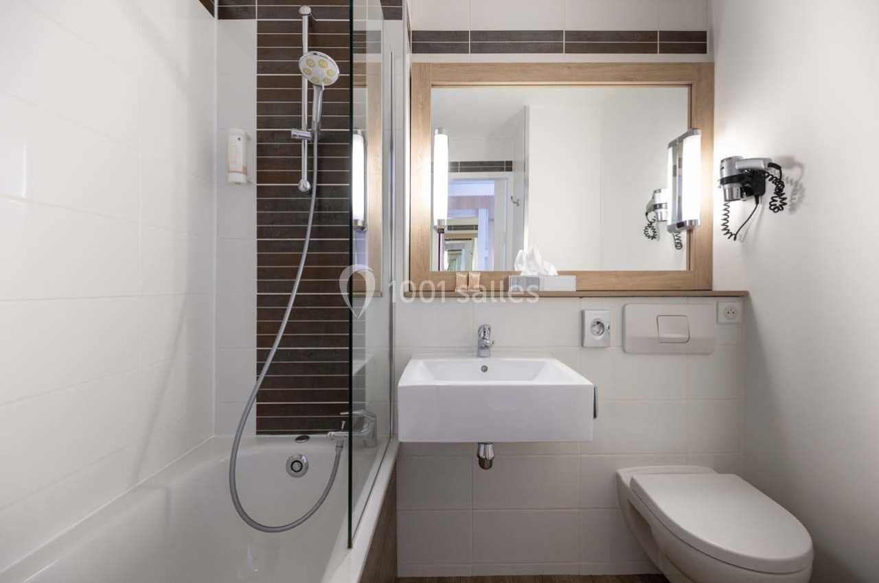 Salle de bain moderne avec baignoire, lavabo, miroir encadré en bois, toilettes et éclairage mural.