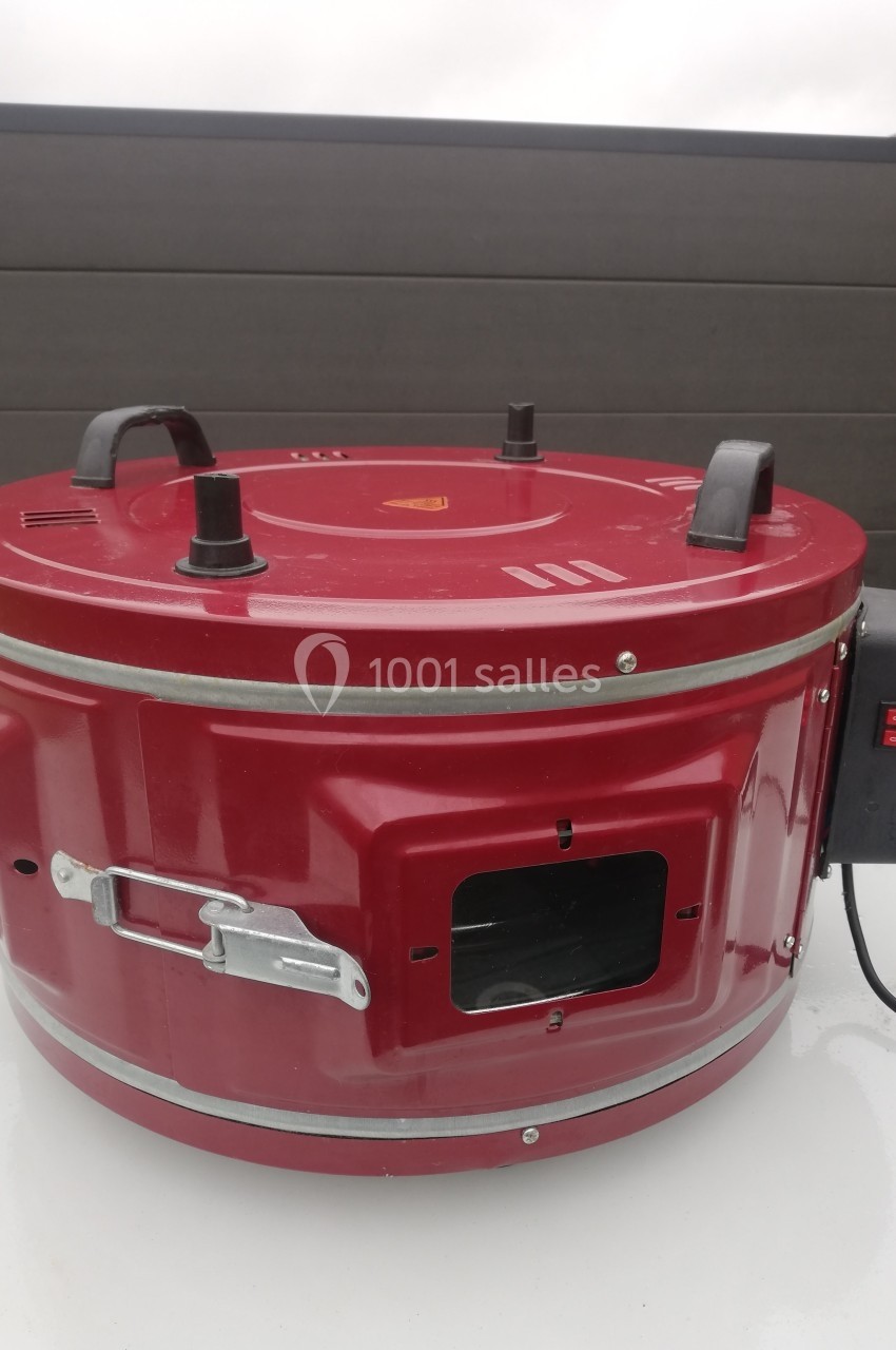 Four électrique portable rouge avec poignées noires, interrupteur latéral et ouverture pour ventilation.