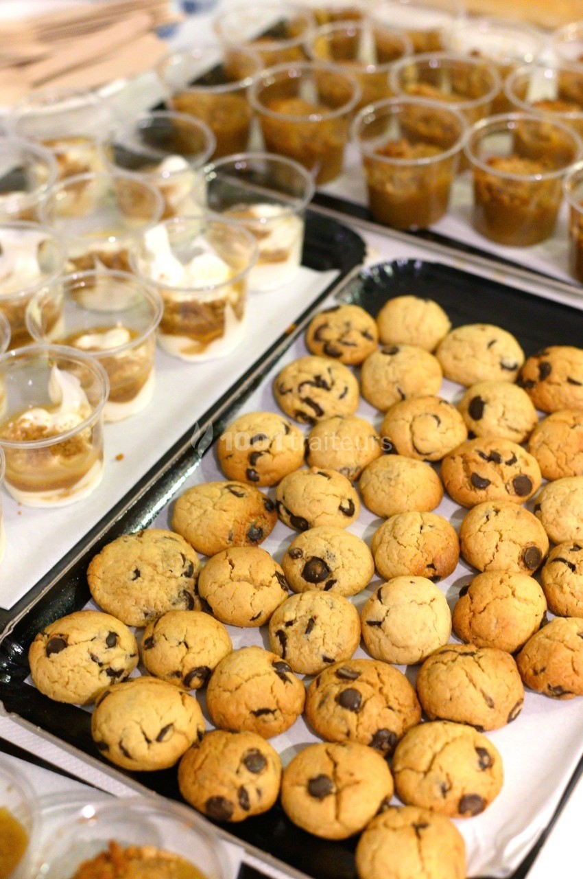 Plateaux de cookies aux pépites de chocolat et verrines de dessert disposés sur une table.