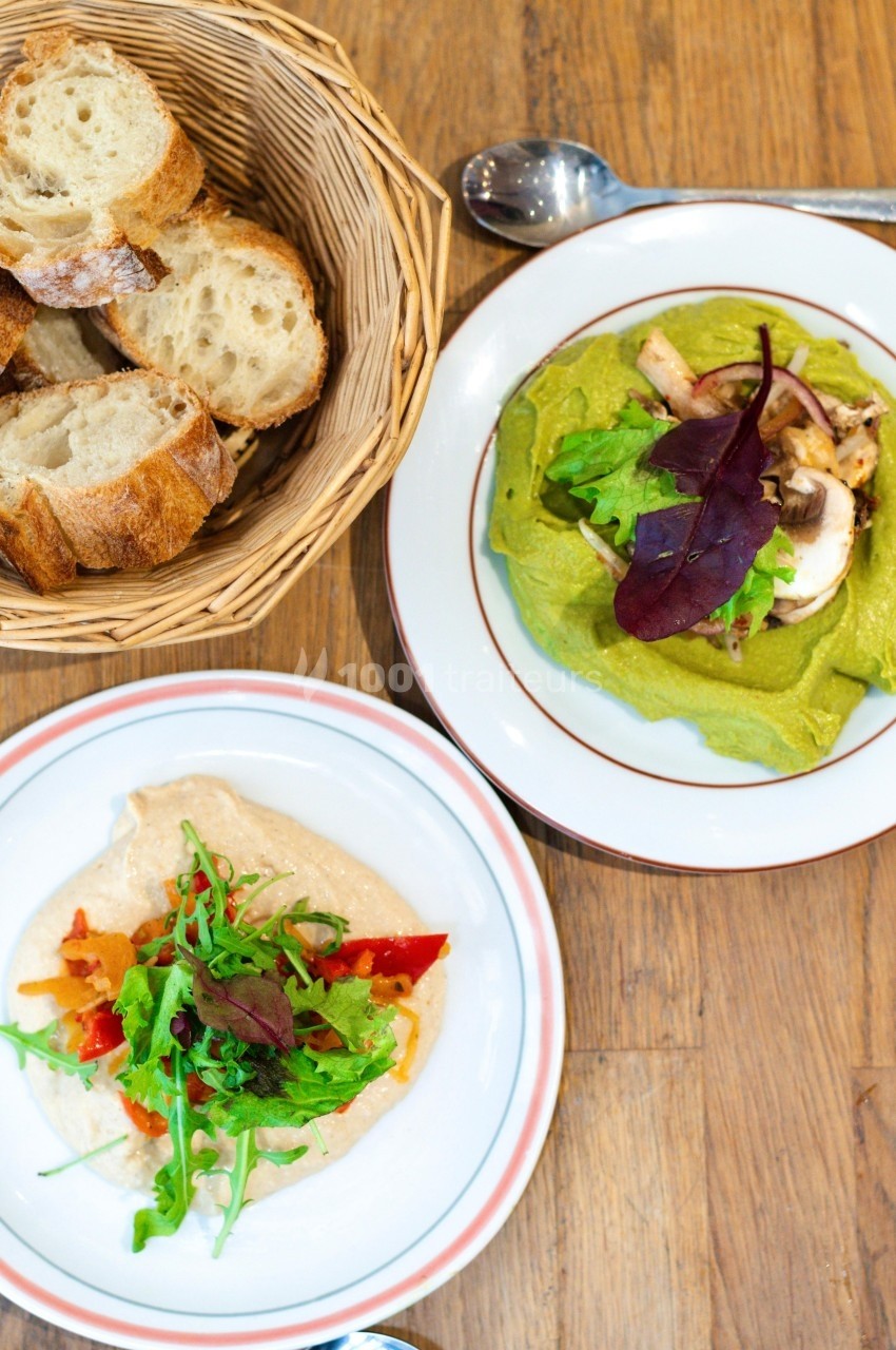 Assiettes de tartines garnies de légumes et salade, accompagnées d'un panier de tranches de pain sur une table en bois.