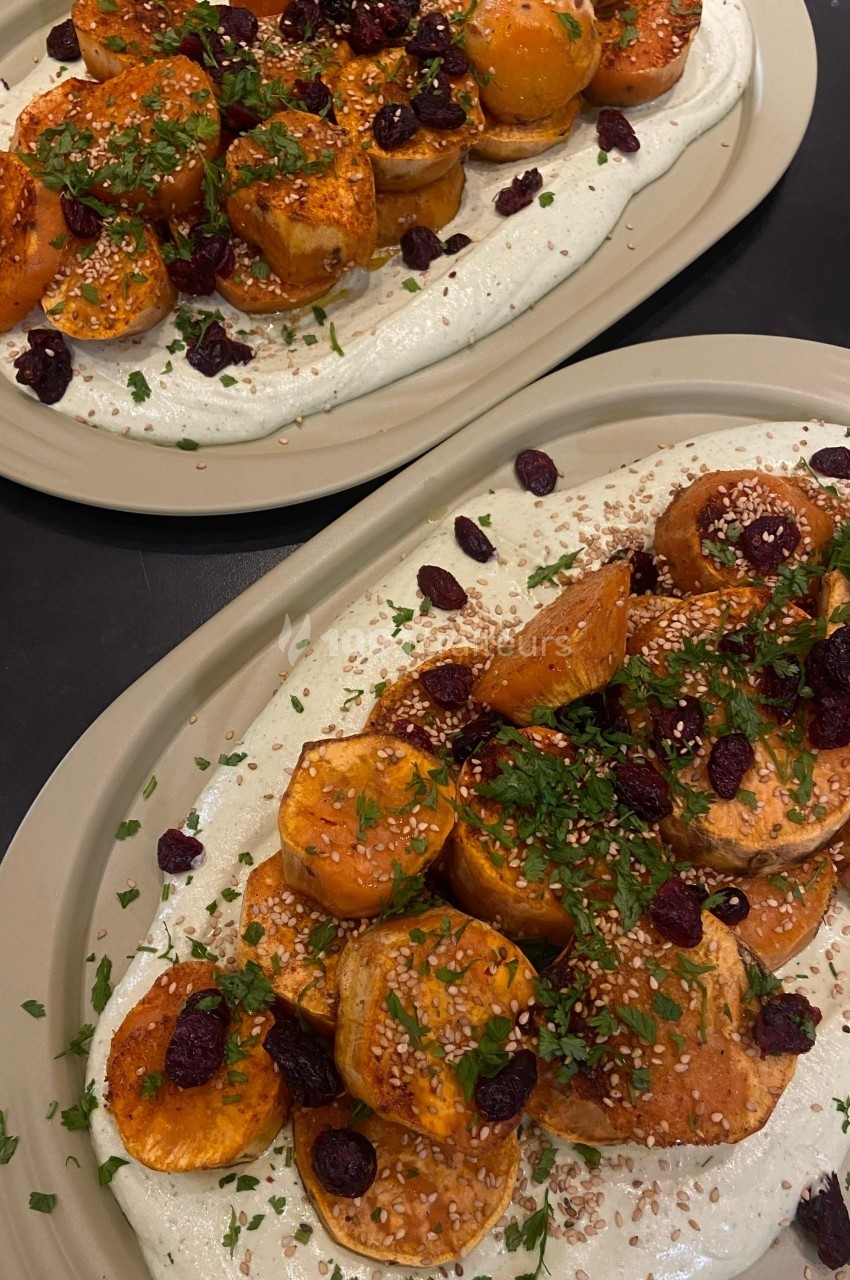 Assiette de légumes rôtis garnis de graines de sésame, herbes fraîches et cranberries sur une base crémeuse blanche.