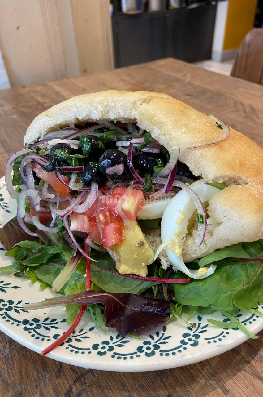 Sandwich pita garni de légumes frais, œufs durs, olives et avocat, servi sur un lit de jeunes pousses.