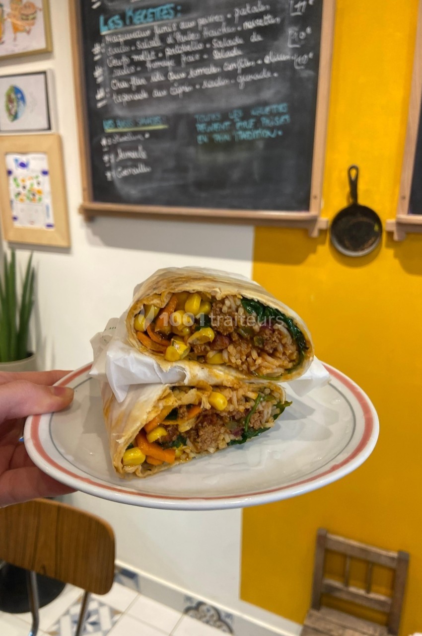 Wrap végétarien garni de légumes, maïs et quinoa, présenté coupé en deux sur une assiette dans un café coloré.