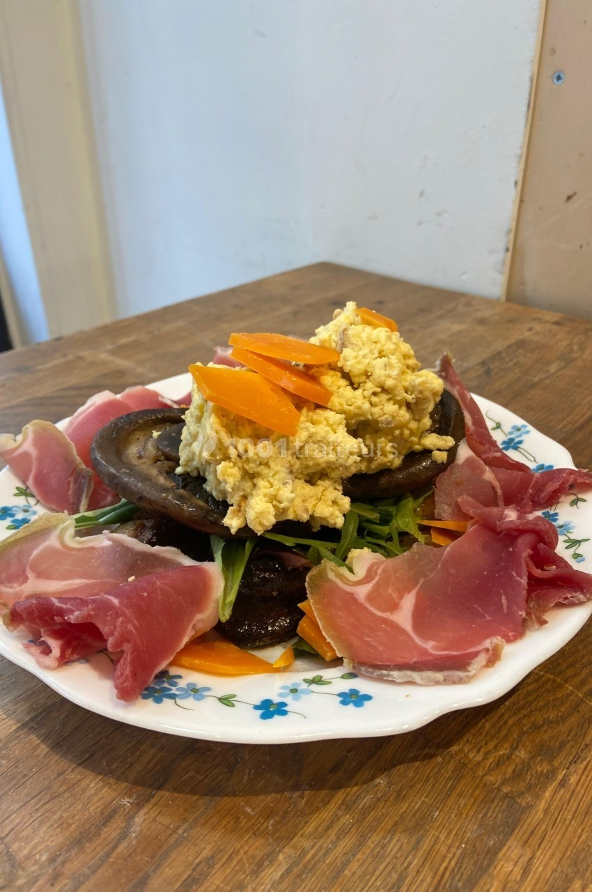 Assiette garnie de jambon cru, champignons, roquette, carottes et œufs brouillés, présentée sur une table en bois.