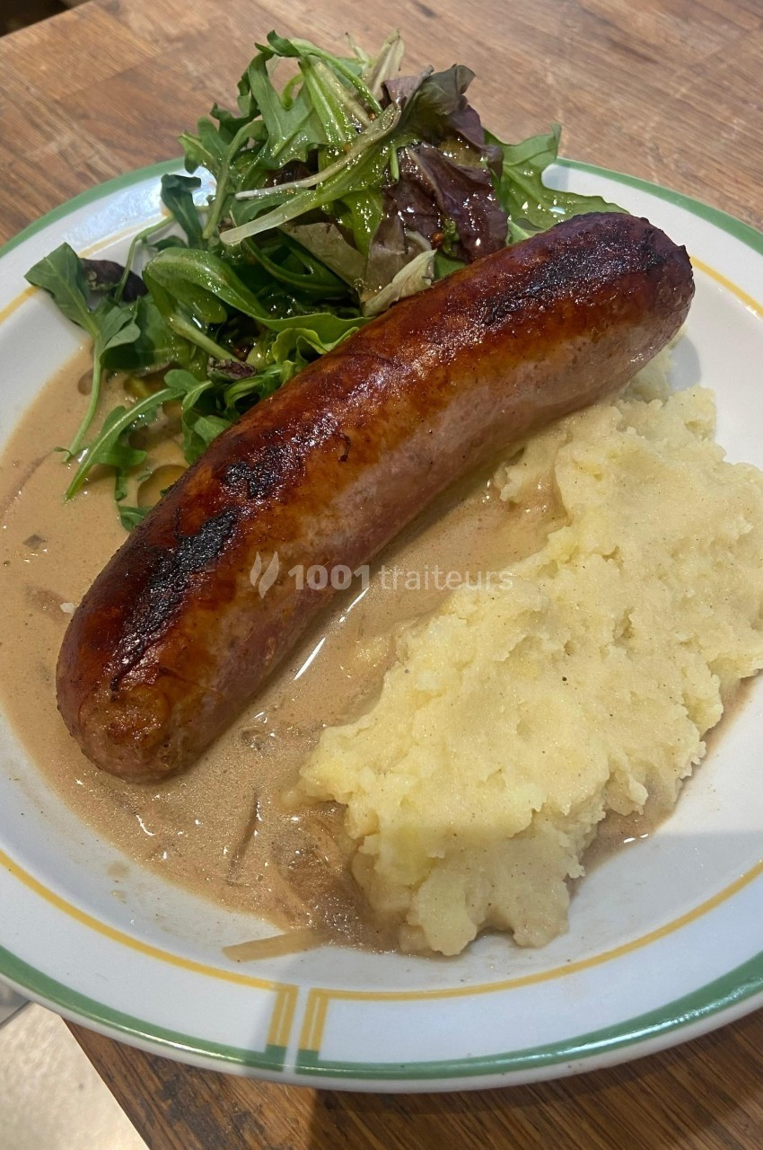 Assiette contenant une saucisse grillée, une purée de pommes de terre, une sauce brune et une salade verte.