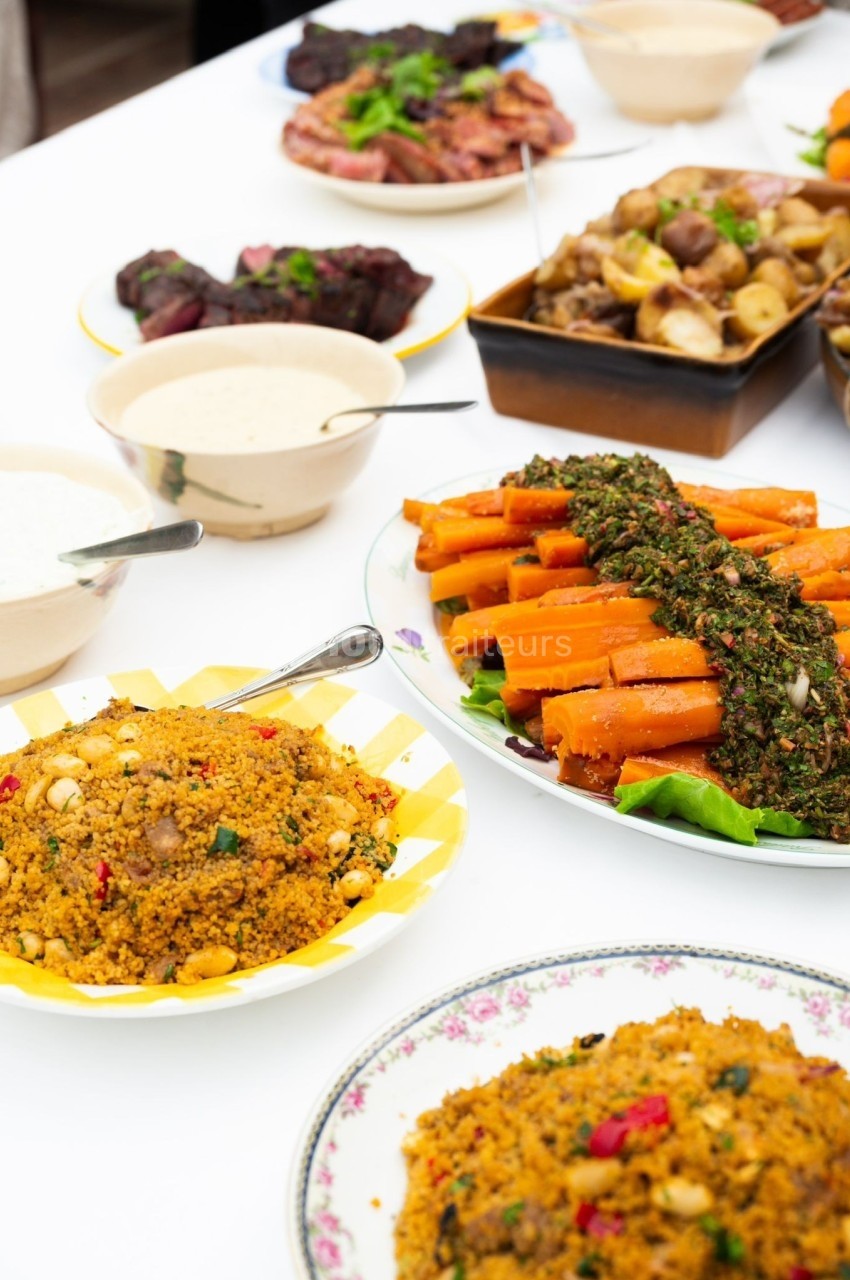 Assortiment de plats sur une table, incluant du couscous, des carottes garnies et diverses sauces.